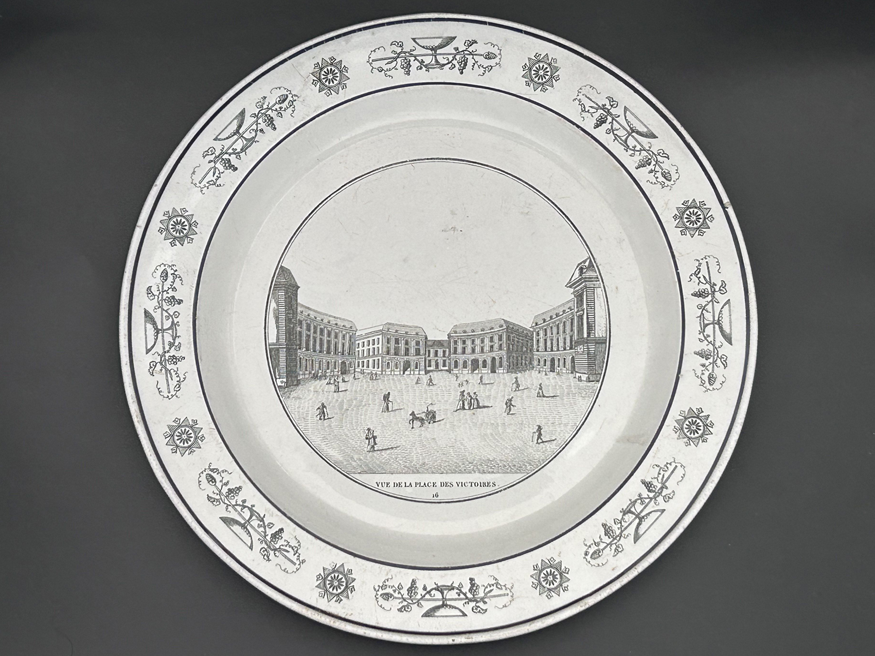 Assiette Vue de la Place des Victoires, XIXe : Assiette en faïence fine avec décor central représentant la place des Victoires à Paris, XIXe